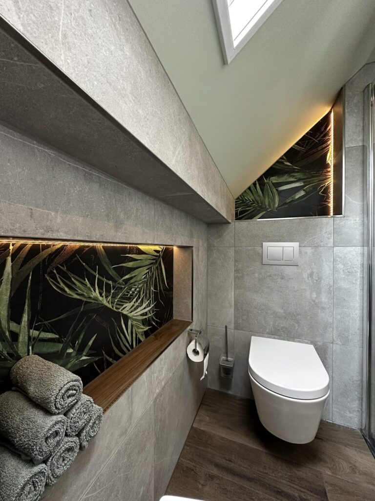 Zolderbadkamer met hangend toilet en verlichte nis met botanische print