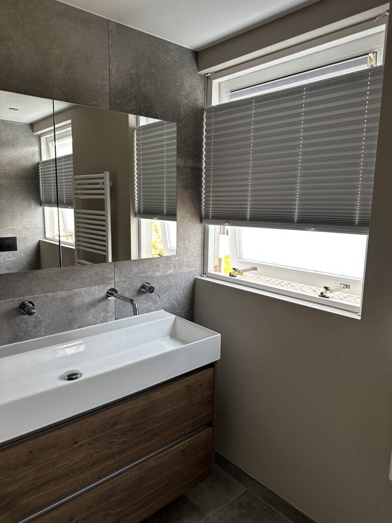 Wastafel met houten badmeubel en spiegelkast in een badkamer met betonlook tegels