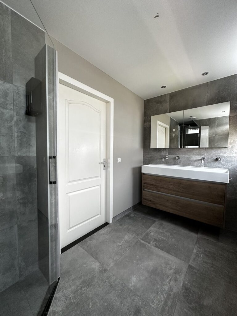 Badkamer met dubbele wastafel, glazen douchewand en betonlook vloer