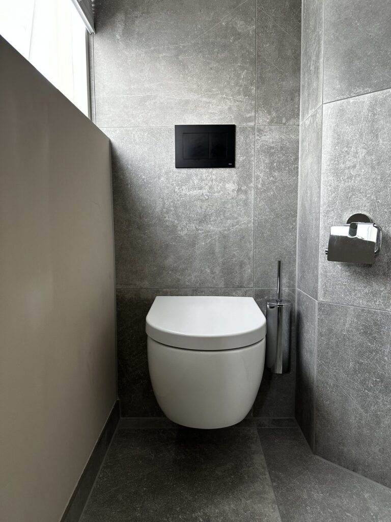 Toilet met zwarte bedieningsplaat en betonlook tegels
