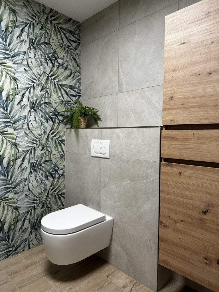 Hangend toilet naast een hoge eiken kast in een badkamer met bladprint wandtegels