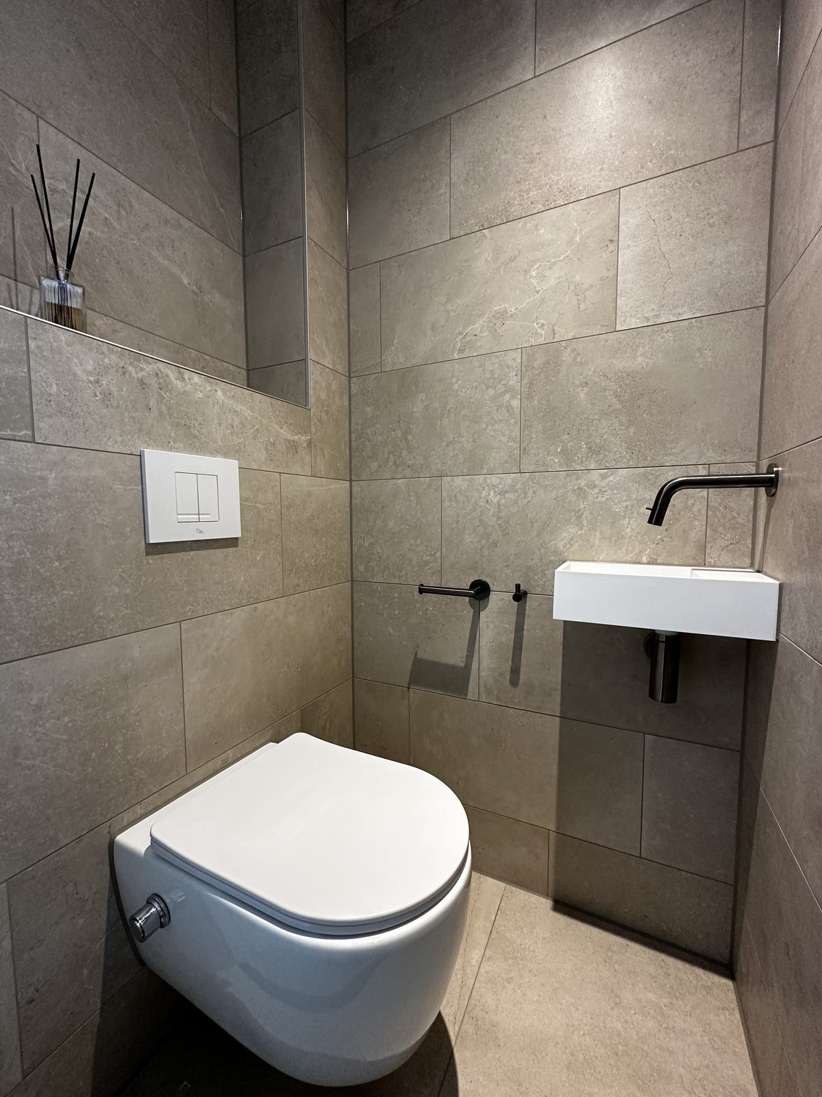 Hangend toilet met fontein in een toilet met natuursteenlook tegels Hangend toilet met fontein in een toilet met natuursteenlook tegels