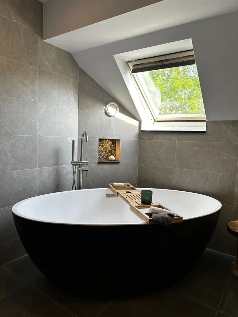 Vrijstaand zwart bad met houten badplank onder het dakraam (Luxe badkamer met groene tegels)